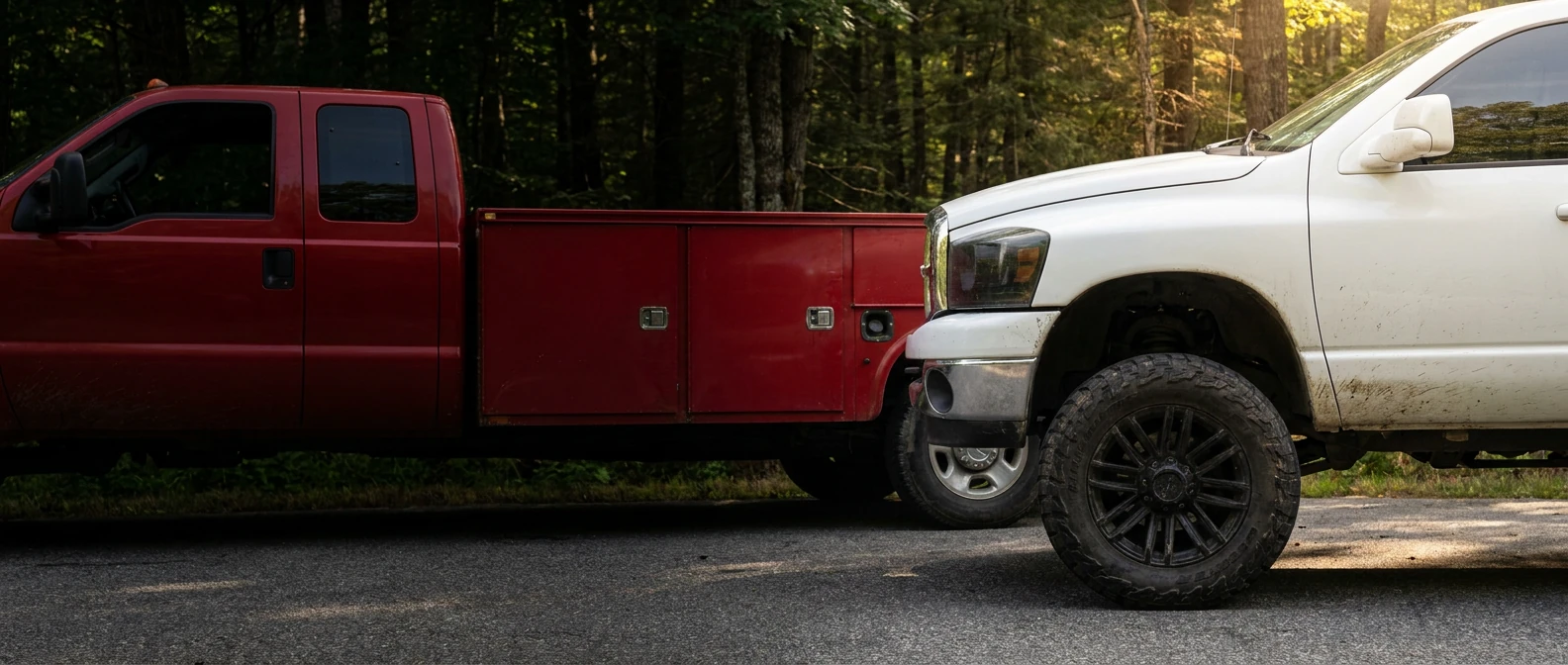 White pickup wheel beside a red service truck at a shaded Maine turnout
